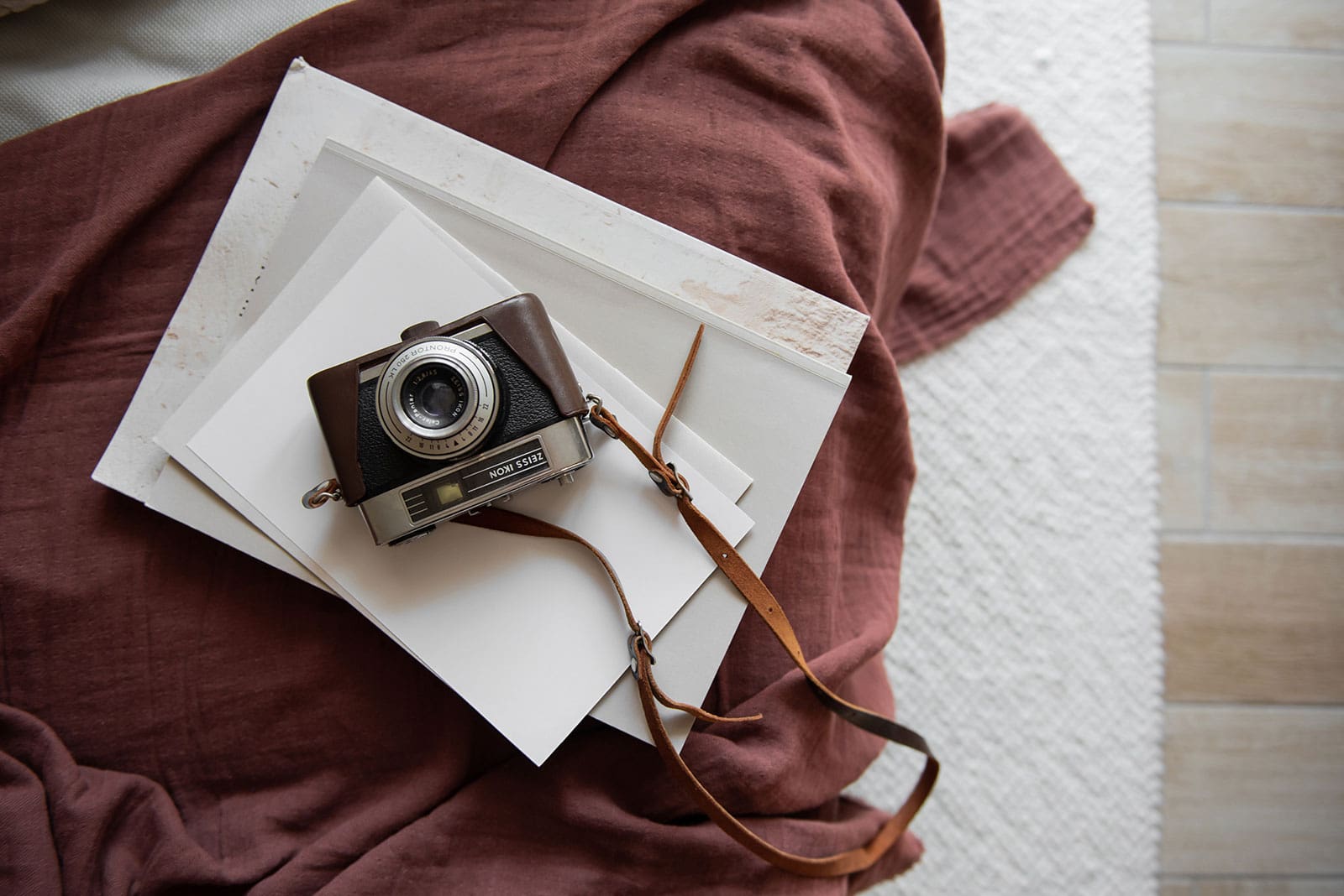 Flatlay of a vintage camera with leather strap resting on layered paper and textured fabric, symbolizing creativity, process, and the evolution of artistic work.