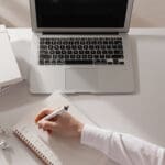 Business owner reviewing notes on how to handle client complaints and writing in planner at desk while analyzing client complaints and strategy.