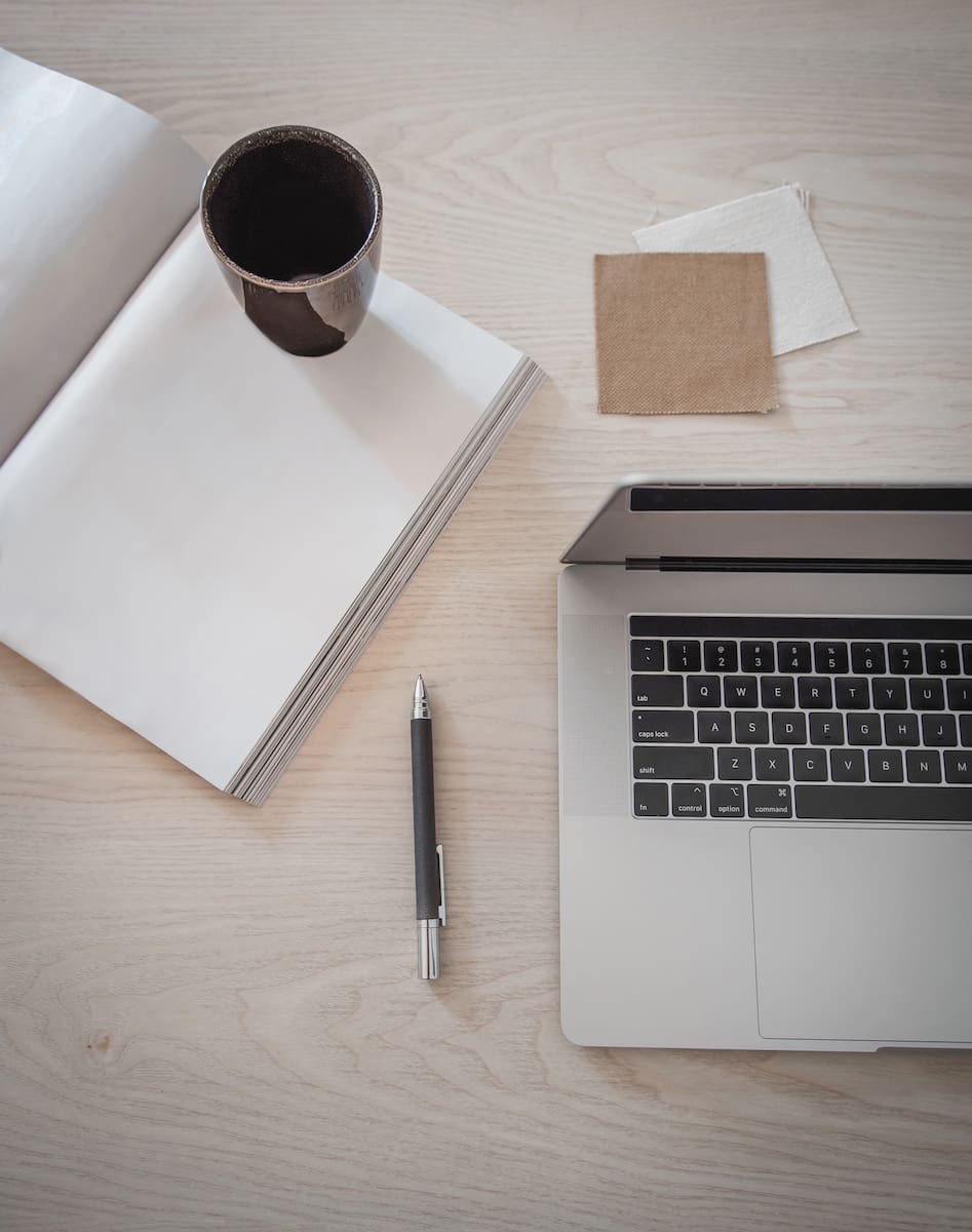 Flat lay of laptop, notebook, pen, and coffee cup on light desk representing small business website planning.