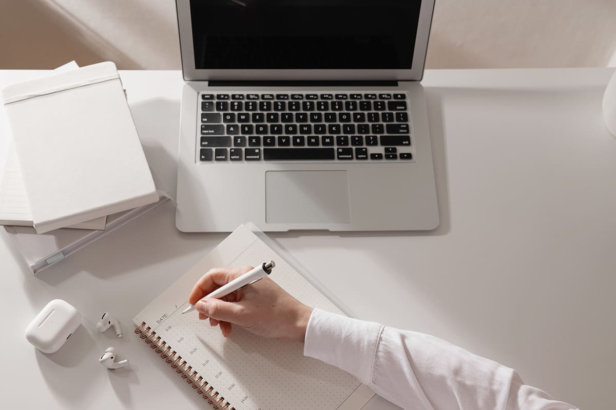 Business owner reviewing notes and writing in planner at desk while analyzing client complaints and strategy.